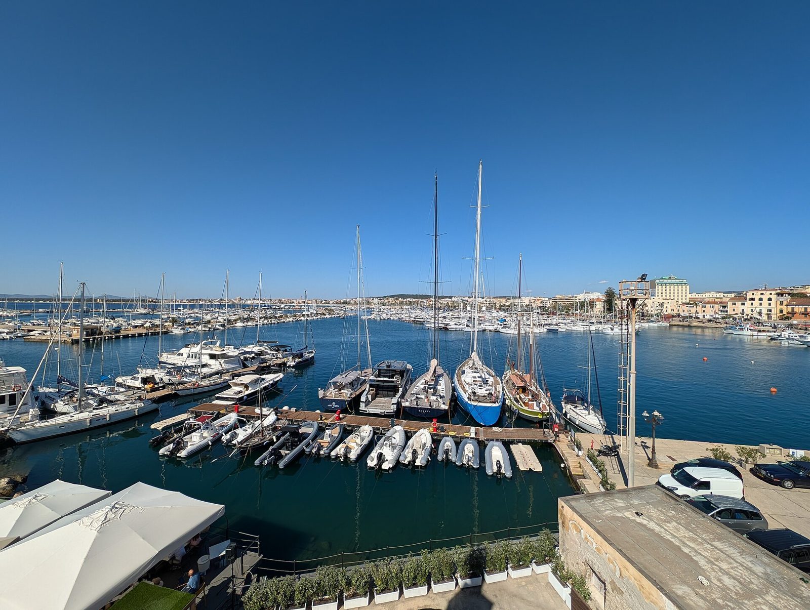 Il porto di Alghero con barche a vela e motoscafi ormeggiati ai pontili sotto un cielo limpido