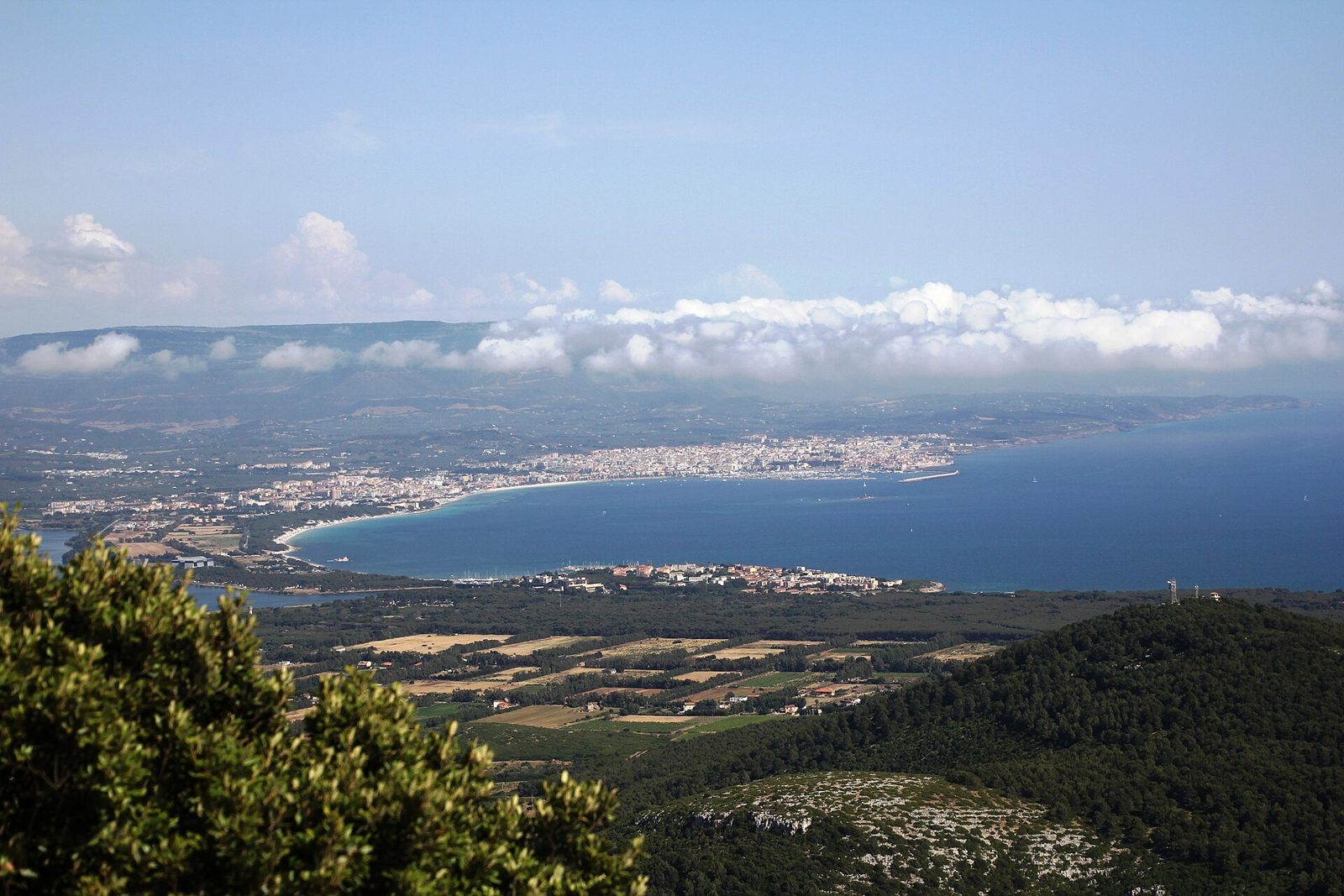Panorama dall'alto del golfo di Alghero e della Riviera del Corallo, con nuvole sulle colline e mare blu